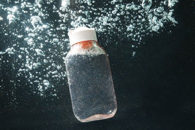 Photo of Bottle of micellar water in liquid with bubbles on black background