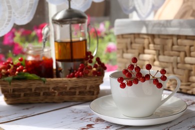 Photo of Cup of hot drink and viburnum berries on white wooden table indoors