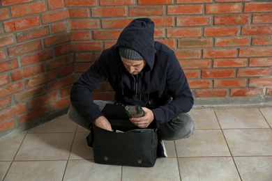 Drug dealer with narcotics sitting on floor against brick wall