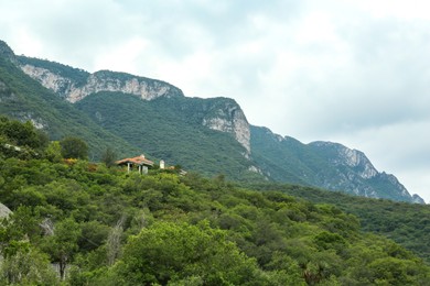 Picturesque view of estate near big mountains and trees under cloudy sky