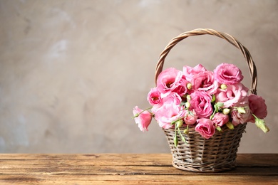 Beautiful pink Eustoma flowers in wicker basket on wooden table against grey background. Space for text