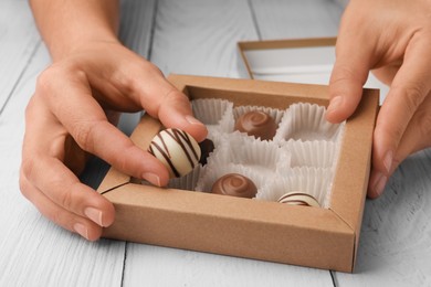 Photo of Woman taking chocolate candy out from partially empty box at white wooden table, closeup