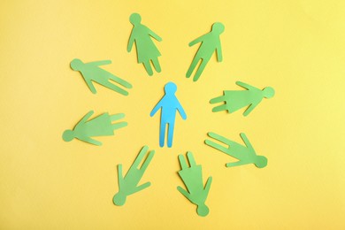 Circle of green paper human figures with blue one in middle on yellow background, flat lay. Diversity and inclusion concept
