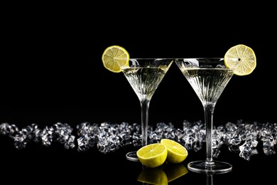 Photo of Two glasses of Martini cocktail and ice cubes on black background, space for text