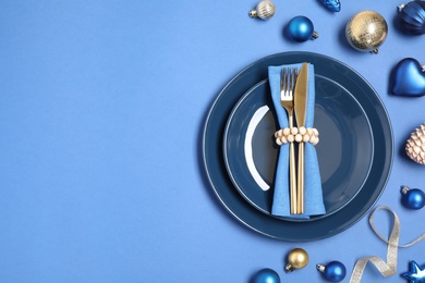 Beautiful table setting with Christmas ornament on blue background, flat lay. Space for text