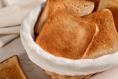 Wicker basket with slices of delicious toasted bread on white wooden table, closeup