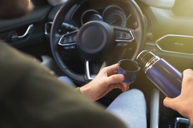 Man with thermos on driver's seat of car, closeup