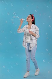 Photo of Young woman blowing soap bubbles on light blue background