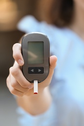 Woman holding digital glucometer on blurred background. Diabetes control