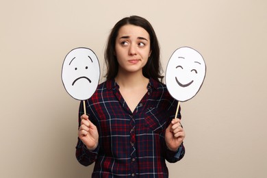 Woman with sad and happy paper faces on beige background