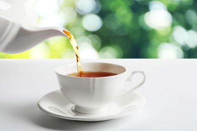 Pouring tea into cup on white table against blurred background