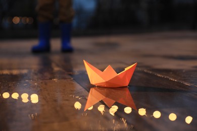 Little boy outdoors, focus on paper boat in puddle