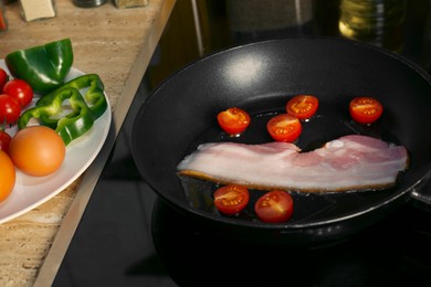 Photo of Cooking bacon with tomatoes in frying pan. Ingredients for breakfast
