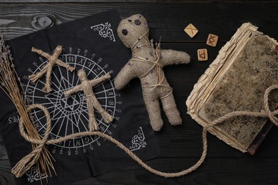 Voodoo doll with pins surrounded by ceremonial items on black wooden table, flat lay