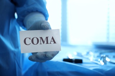 Surgeon holding card with word Coma in hospital, closeup. Space for text