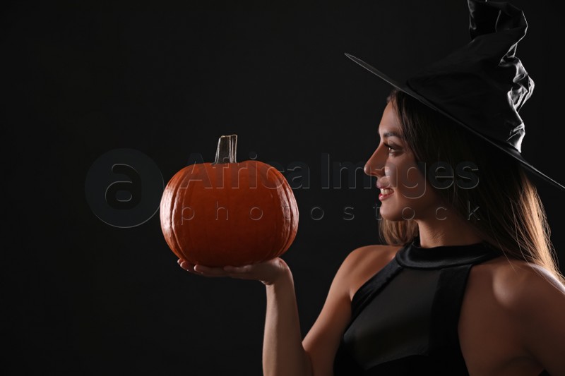 Young woman wearing witch costume with pumpkin on black background. Halloween party