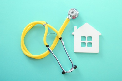 Flat lay composition with house model and stethoscope on color background, top view