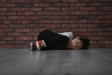 Photo of Sad little girl closing eyes with hands on floor near brick wall. Child in danger