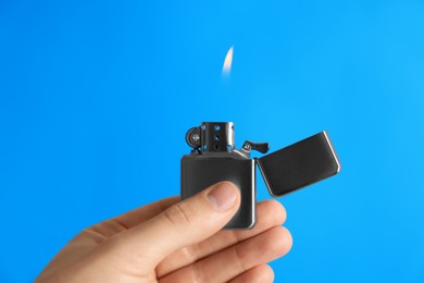 Photo of Man holding lighter with burning flame on light blue background, closeup