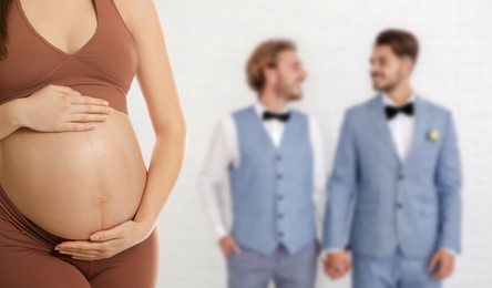 Surrogacy concept. Young pregnant woman and blurred view of happy gay couple on light background