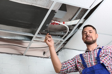 Professional technician repairing ceiling mounted air conditioner indoors