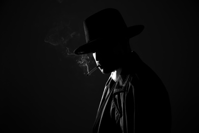 Old fashioned detective smoking cigarette on dark background, black and white effect