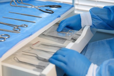 Doctor putting Pott's scissors into drawer indoors, closeup. Table with different surgical instruments