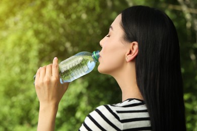 Beautiful young woman drinking water outdoors. Refreshing drink