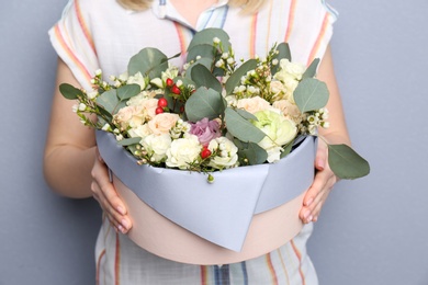 Female florist holding box with flowers on grey background