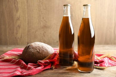 Photo of Bottles of delicious fresh kvass, spikelets and bread on wooden table