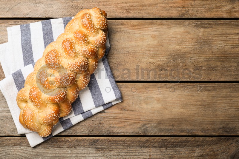 Homemade braided bread with sesame seeds on wooden table, top view and space for text. Traditional Shabbat challah