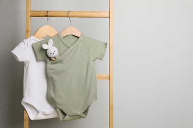 Baby bodysuits hanging on ladder near light wall, space for text