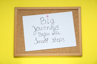 Photo of Corkboard with pinned message Big Journeys Begin With Small Steps on yellow background, top view. Motivational quote