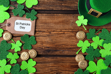 Frame made of clover leaves and gold coins on wooden table, flat lay with space for text. St. Patrick's Day celebration
