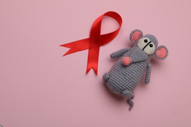 Photo of Cute knitted toy mouse and red ribbon on pink background, flat lay with space for text. AIDS disease awareness