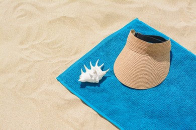 Photo of Towel, straw visor cap and seashell on sand, space for text. Beach accessories