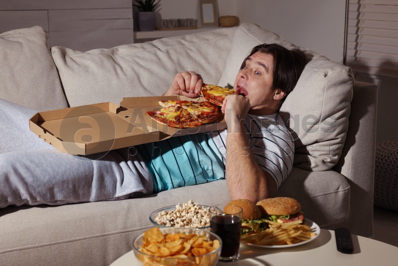 Overweight man eating pizza on sofa at home
