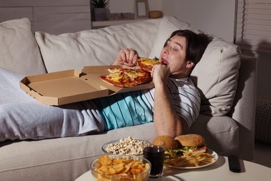 Photo of Overweight man eating pizza on sofa at home