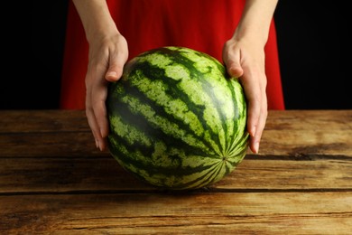 Woman with delicious ripe watermelon at wooden table against black background, closeup