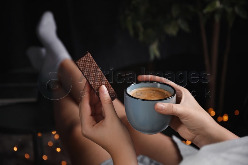 Woman with wafer and coffee on dark background, closeup. Early breakfast