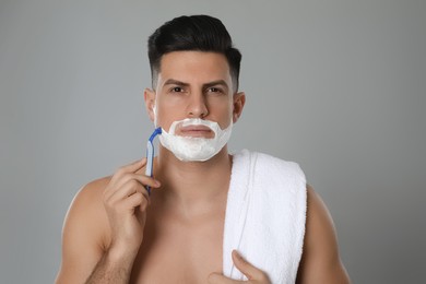 Handsome man shaving with razor on grey background