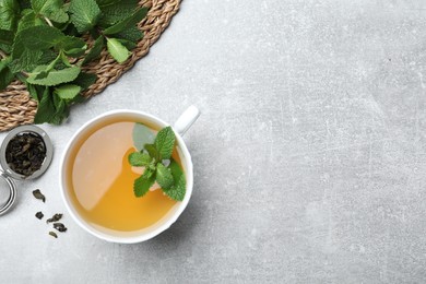 Photo of Cup of aromatic green tea with mint and dry leaves on grey table, flat lay. Space for text