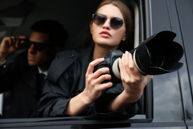 Private detectives with modern camera spying from car, focus on lens