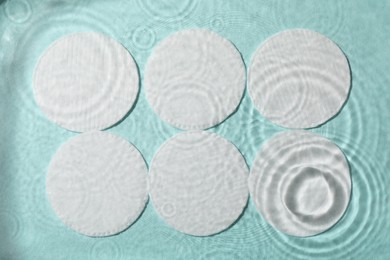 White cotton pads in water on turquoise background, flat lay