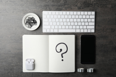 Notebook with question mark, smartphone and keyboard on grey table, flat lay