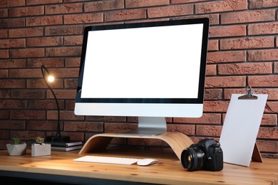Comfortable workplace with modern computer on wooden table near brick wall. Space for text