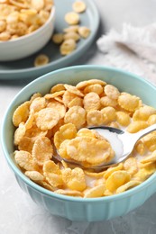 Spoon in bowl with tasty cornflakes and milk on table, closeup