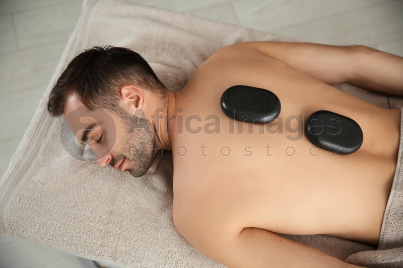 Photo of Handsome man receiving hot stone massage in spa salon, top view