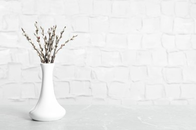 Beautiful pussy willow branches in vase on grey marble table, space for text