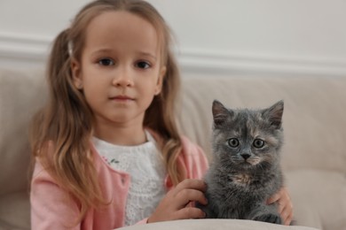 Photo of Cute little girl with kitten on sofa at home. Childhood pet